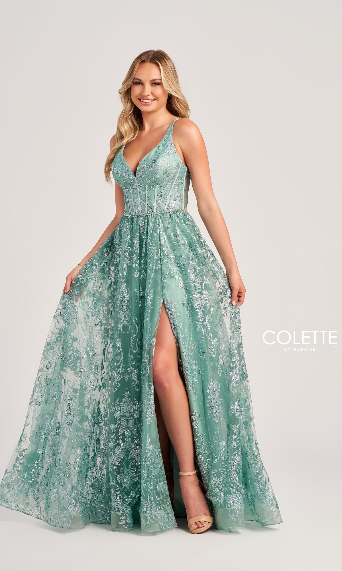 A woman smiles against a plain background, wearing the Glitter-Tulle Colette Long Prom Dress CL5134—an elegant sleeveless, light teal sequin gown with a high slit and corset-style bodice.